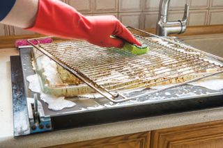 A person wiping a dirty oven rack with a soapy sponge