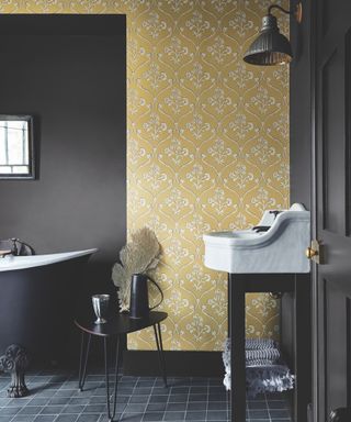 black bathroom with yellow leafy wallpaper on one wall, black tub, black walls and floor,