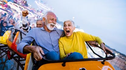 An older couple laugh and scream while on a roller coaster.