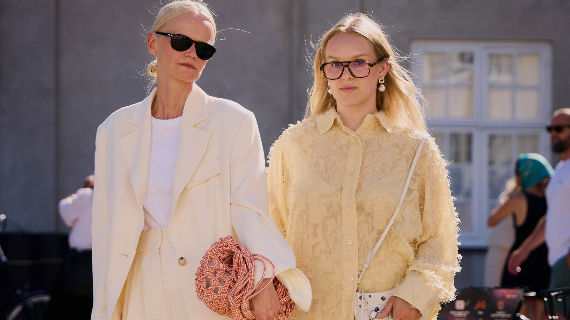 Two women pose. One wearing an all white suit and one wearing a yellow set. 