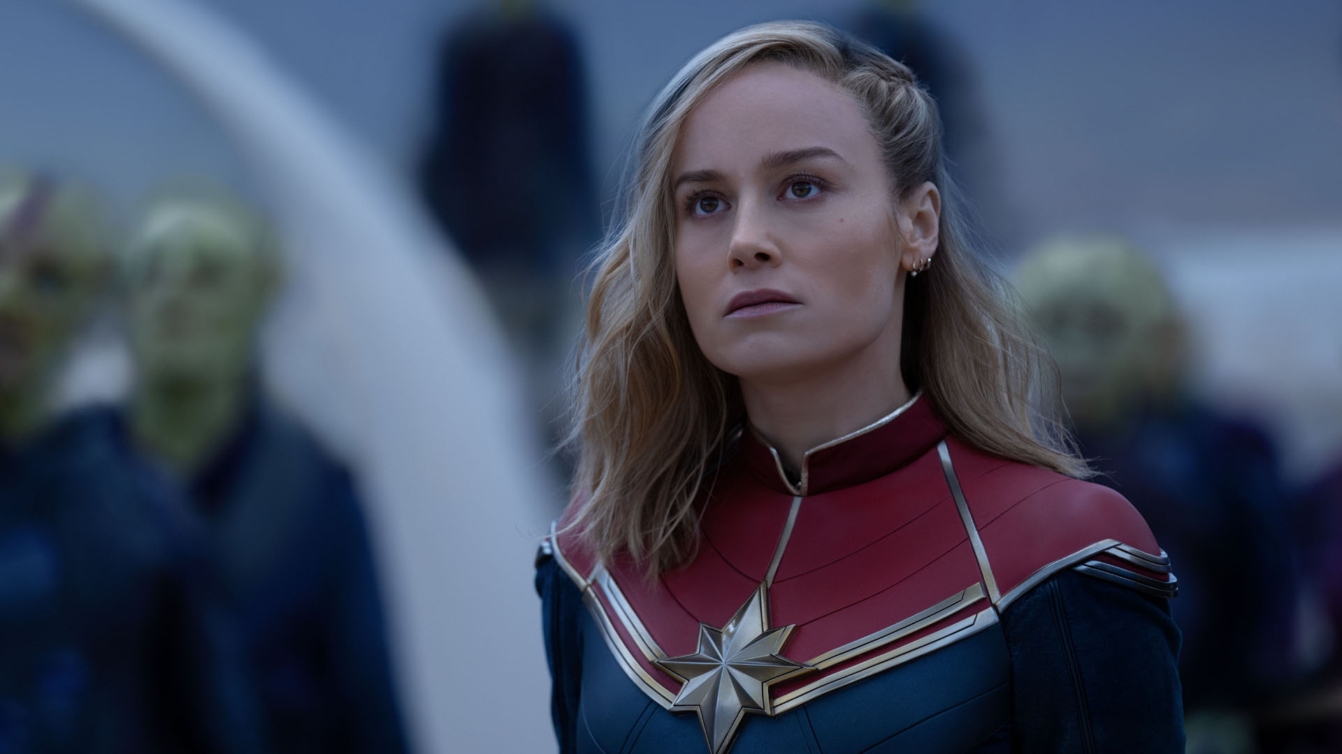 Carol Danvers look at something off-screen with some Skrulls behind her in The Marvels