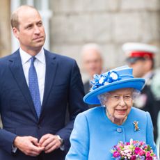 Queen Elizabeth II wears a blue jacket and matching hat and Prince William wears a suit