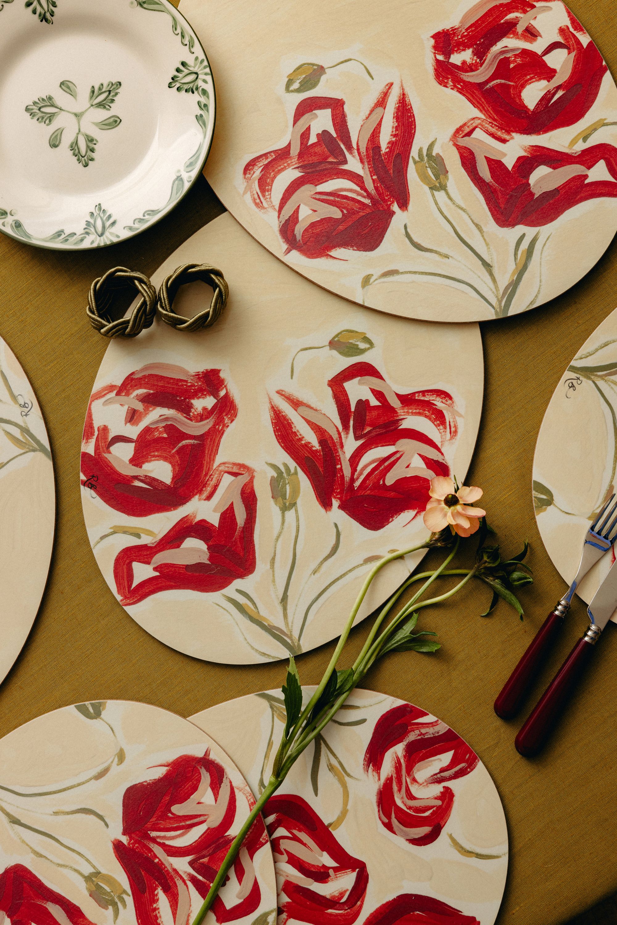 Image of a mustard yellow tablecloth with multiple plate mats that are painted with red flowers.