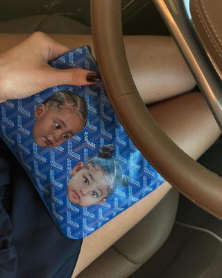 Kylie Jenner wearing a frilly black dress with leather flip flops and a custom blue Goyard wallet painted with Stormi and Airé's faces August 2024