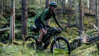 Bikepacker Jenny Tough riding a loaded mountain bike through a forest