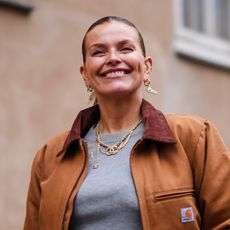 street style shot of woman in grey top and brown jacket smiling