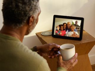 Man holding coffee mug sitting in front of Echo Show on a video conference call