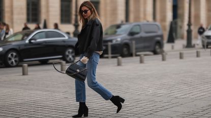 Diane Batoukina @diaanebt wears a white latte cashmere turtleneck pullover from Zara, a black shiny leather with white sheep interior aviator coat from Chanel, blue faded denim large mom jeans pants, during a street style fashion photo session, on November 10, 2021 in Paris, France.