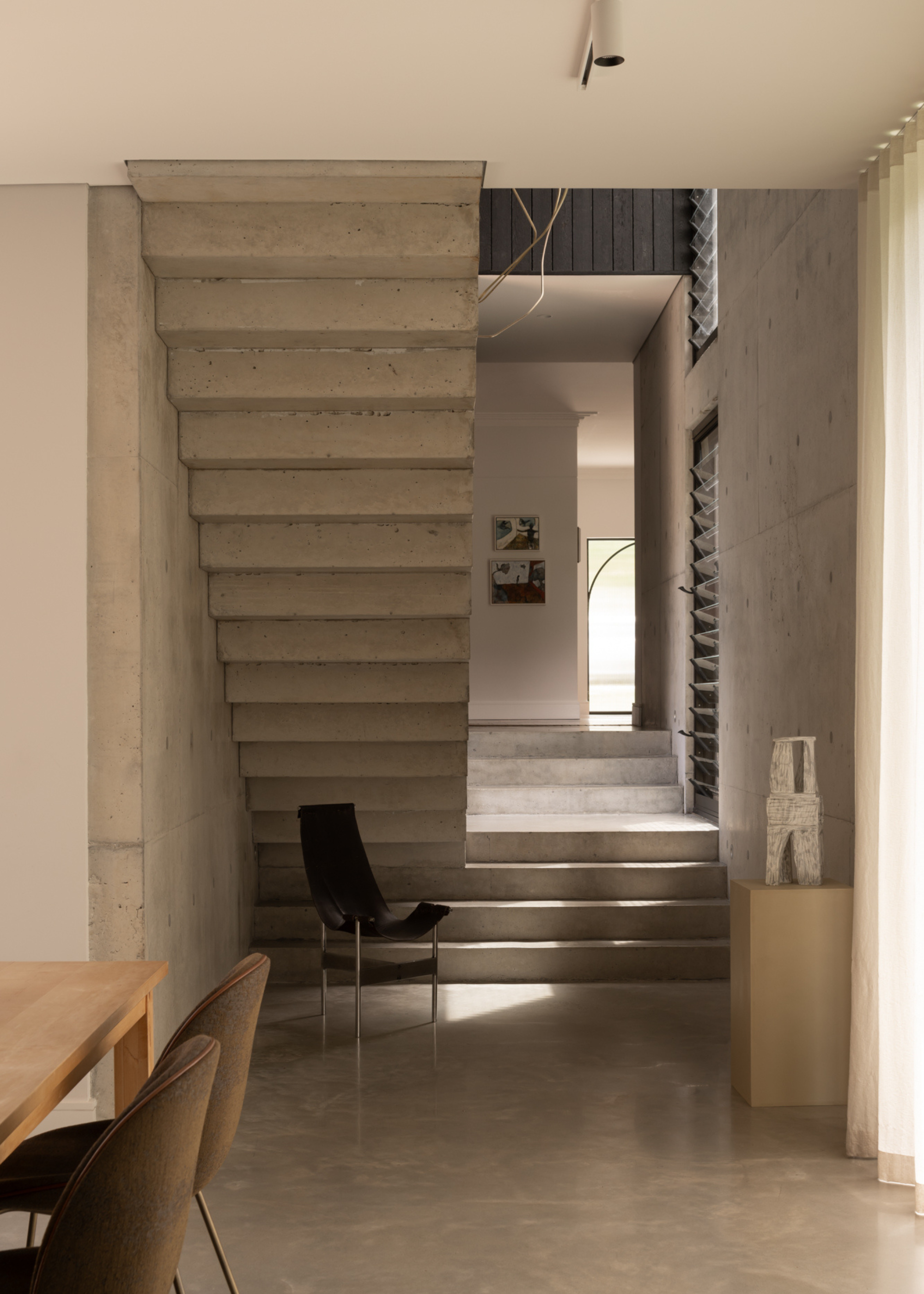 An entryway by a set of cement stairs, a leather chair, and a plinth with a vase