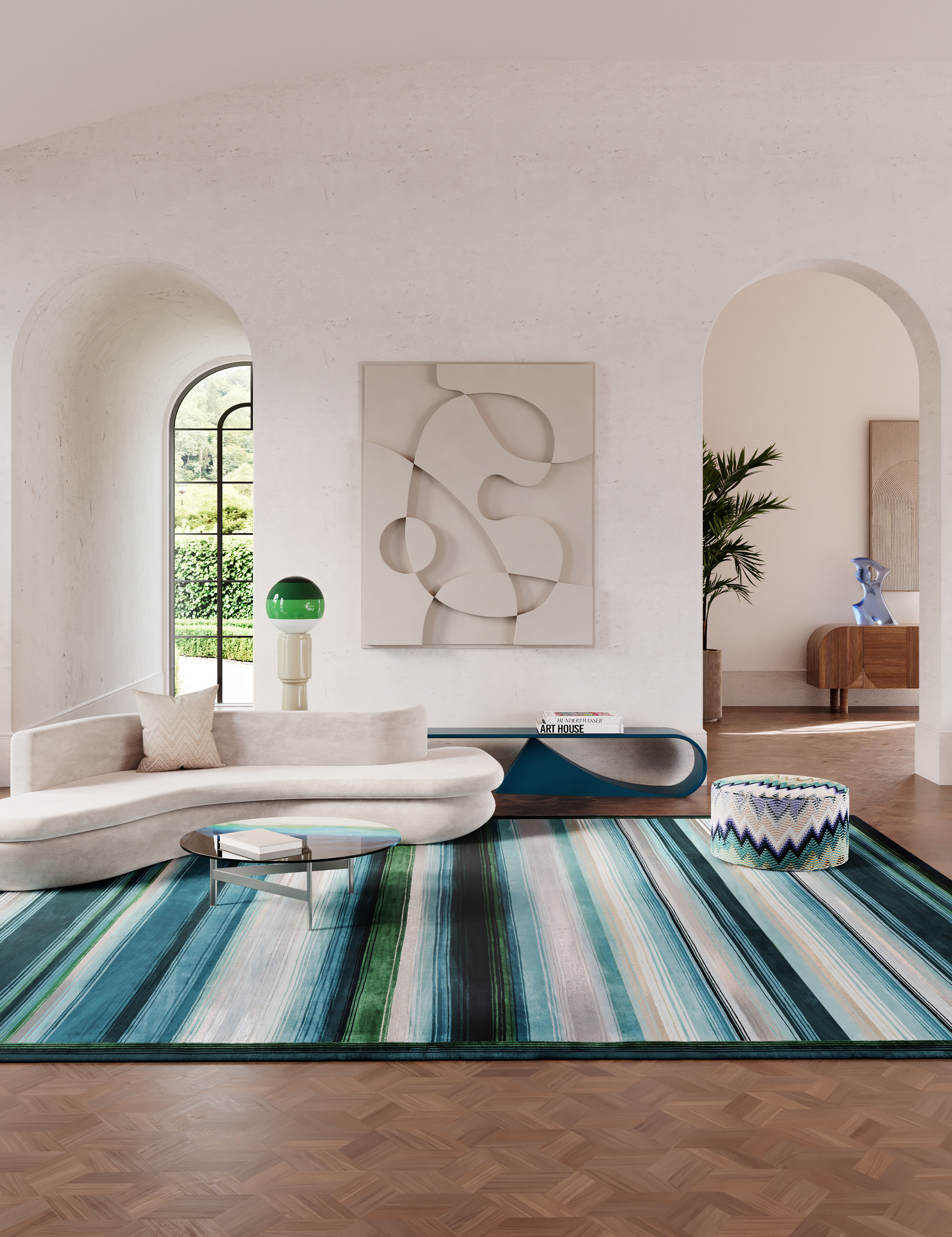 Image of a white living room with high ceilings and curved archways. There is a curved, white sofa positioned on a blue, white, and green striped rug. There is a coffee table in front of the sofa and a blue console table on the back wall.