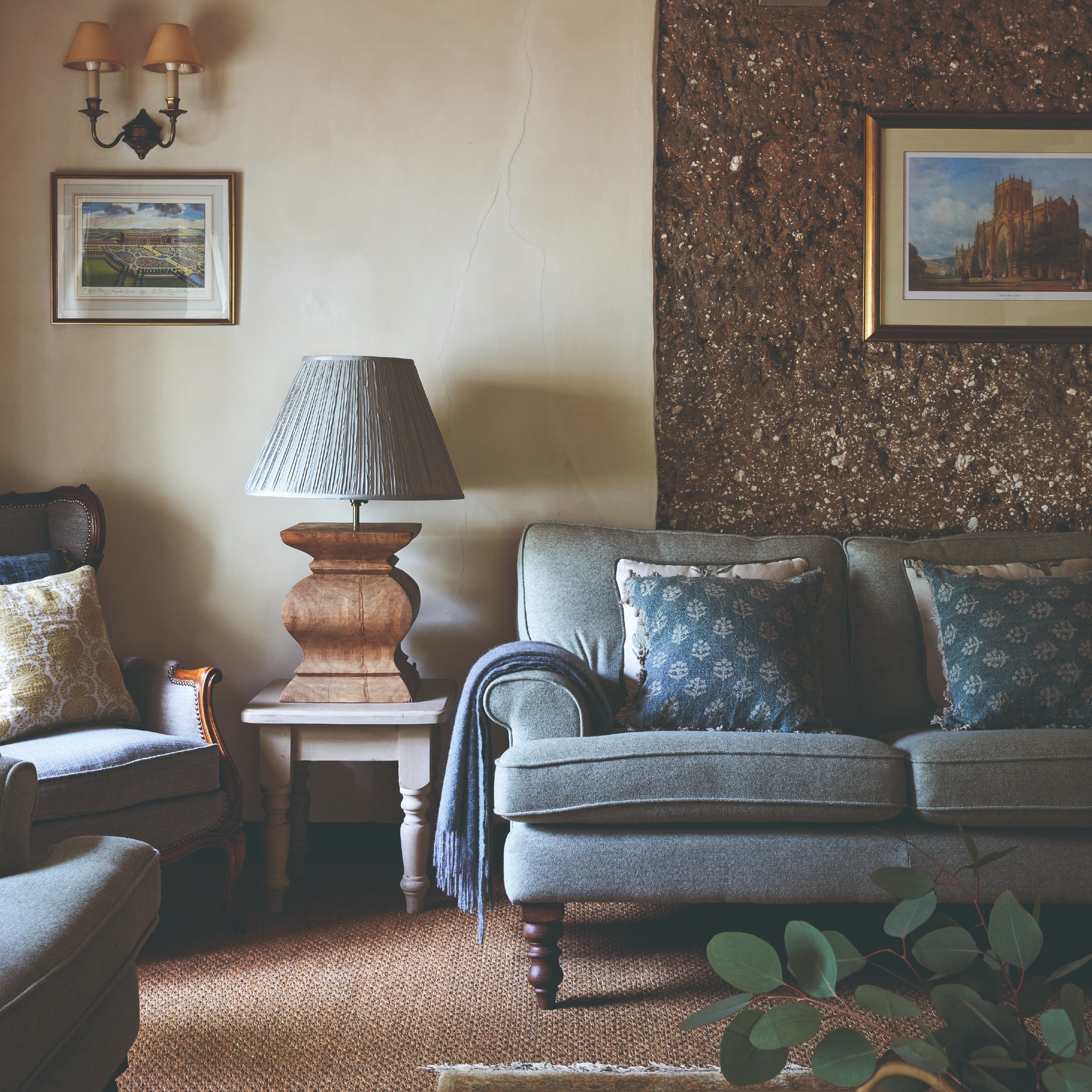 A living room with a traditional-style blue sofa, an oversized table lamp on a side table next to it and a wall light