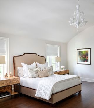 bedroom with French-style bed and upholstered bedhead and neutral linens, pale walls and white chandelier