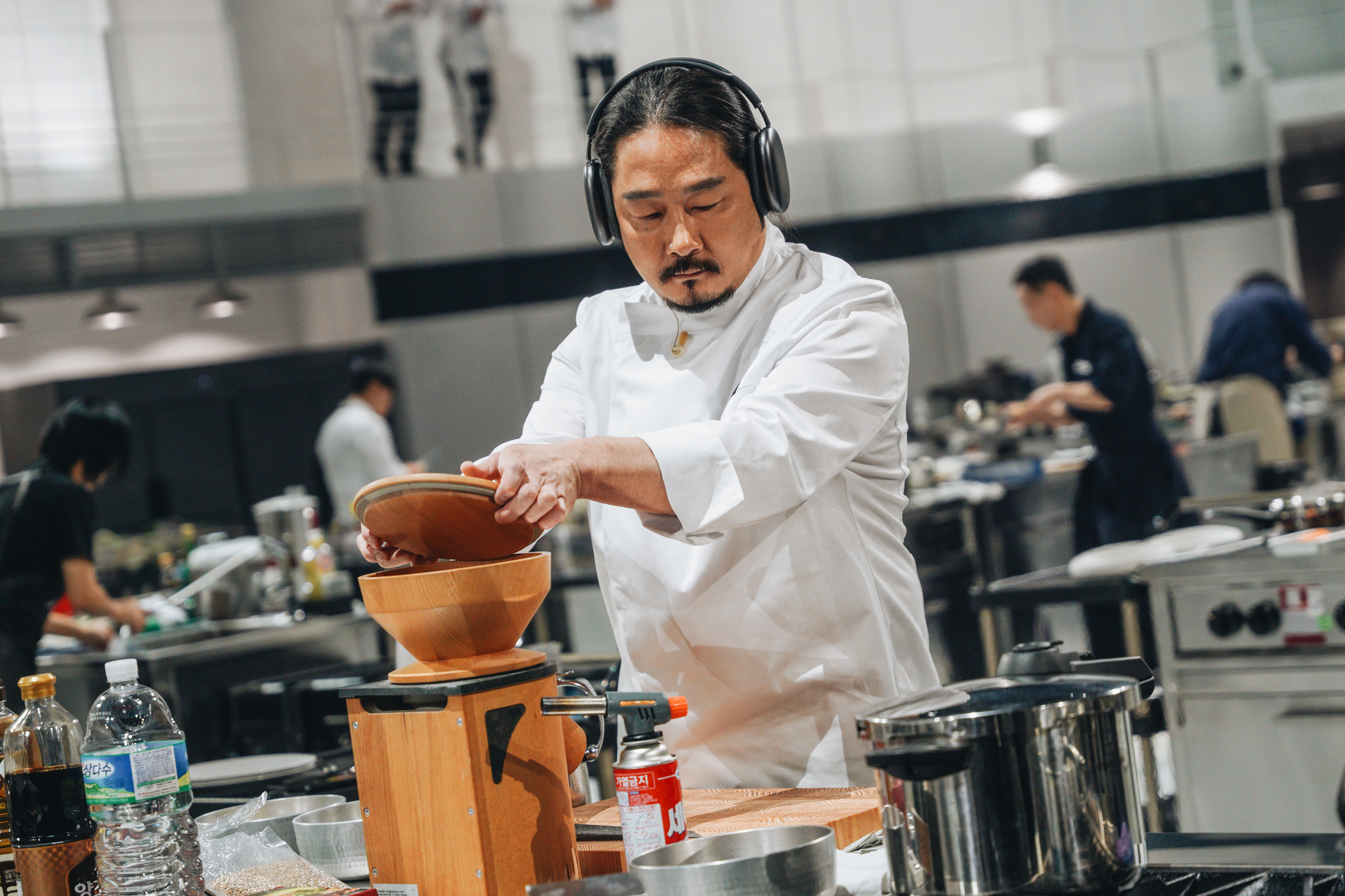A chef (Kim Do-yun) wears headphones as he cooks at a work station, in 'Culinary Class Wars' season 2.