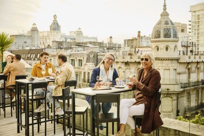Wide shot of smiling senior women enjoying dinner and drinks at a luxury hotel rooftop restaurant during vacation to Buenos Aires.