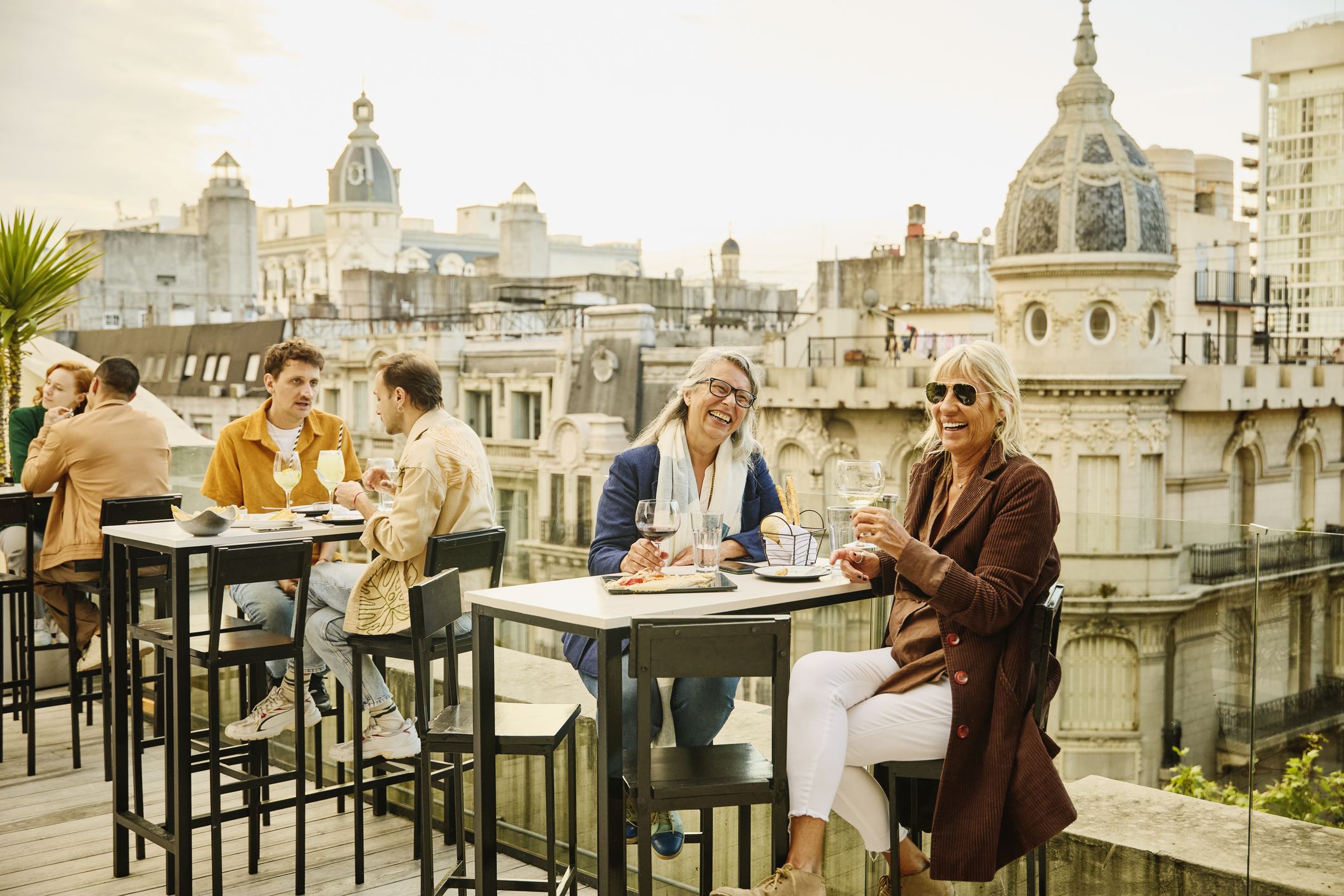 Wide shot of smiling senior women enjoying dinner and drinks at a luxury hotel rooftop restaurant during vacation to Buenos Aires.