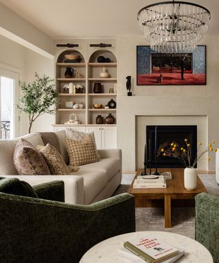 A white living room with arched built-in cabinets, green armchairs, a fireplace, and a circular chandelier