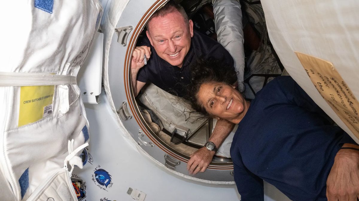 Two smiling astronauts pose in a circular doorway on the International Space Station