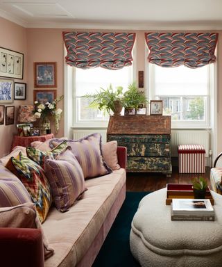 pastel living room ideas, pastel pink living room with pink couch, patterned blinds, bright cushions, old vintage writing desk, artwork, plants