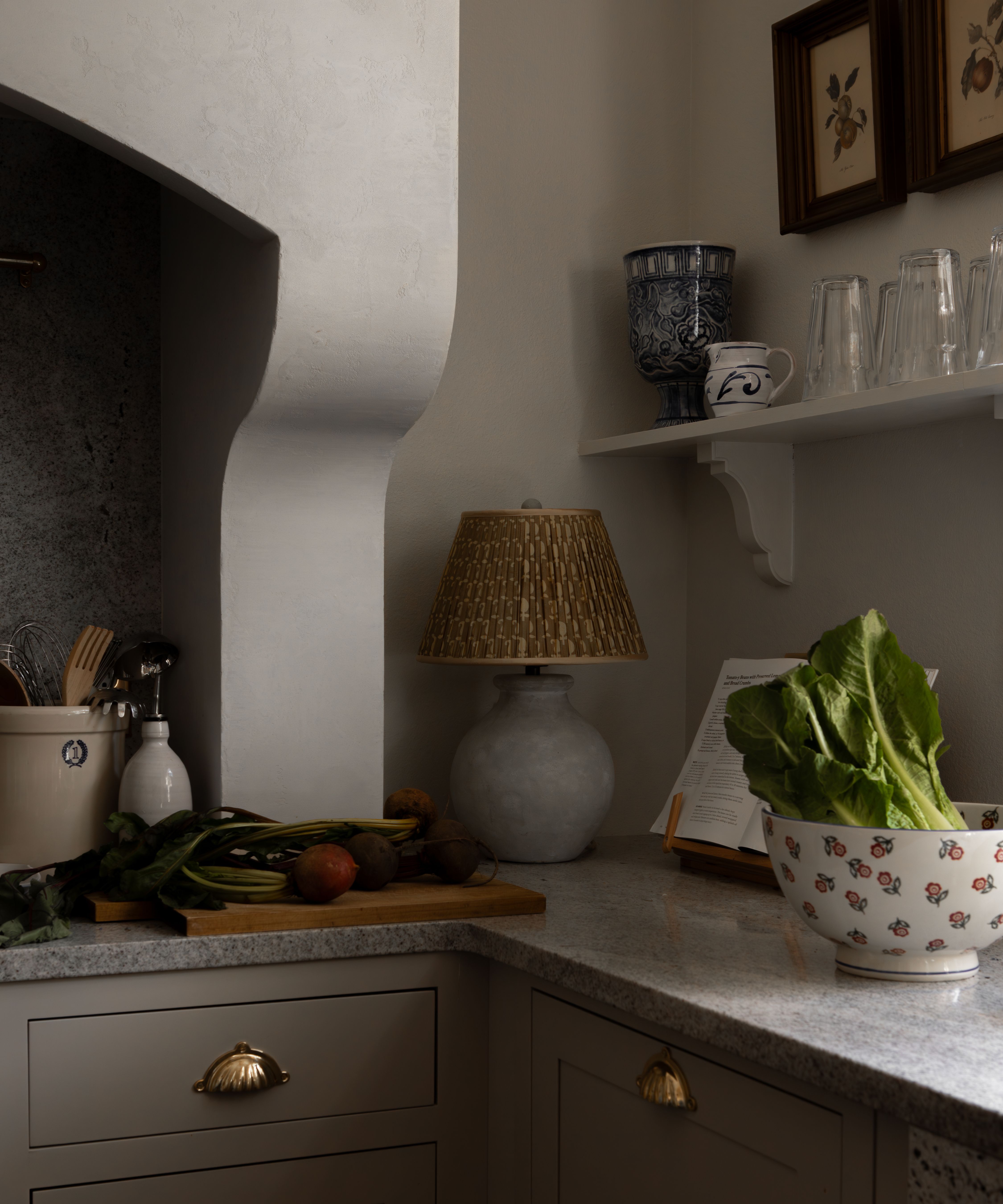 the corner of a cozy neutral kitchen with granite counters and a large plaster cooker hood
