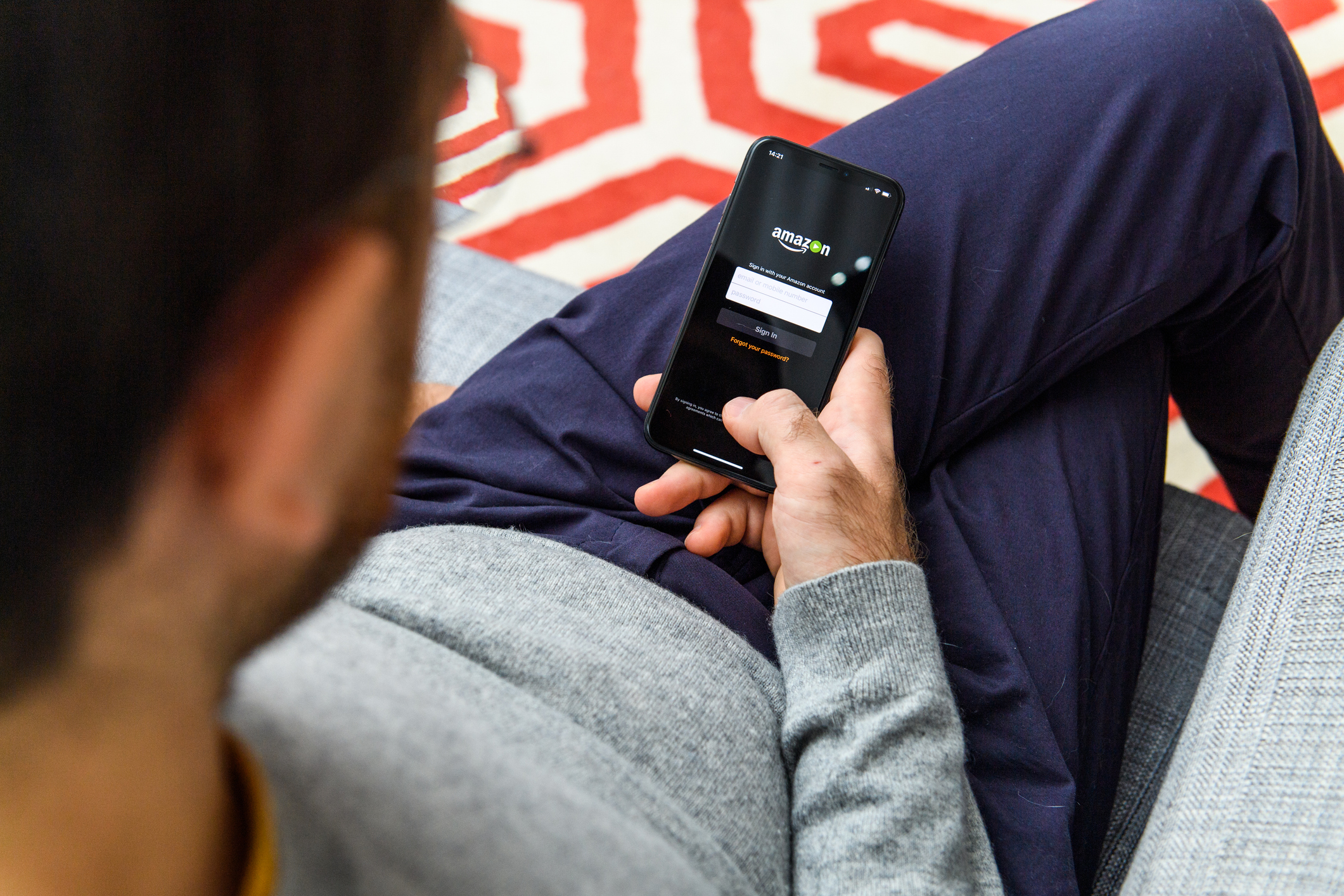 Man logging into Amazon on his mobile phone while sitting on a couch.