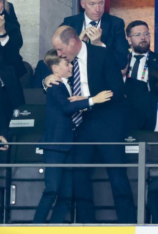 Prince George wearing a suit and tie hugging his dad Prince William at the 2024 Euros final game