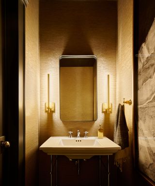 A powder room with dramatic lighting, a large mirror, and two gold light fixtures