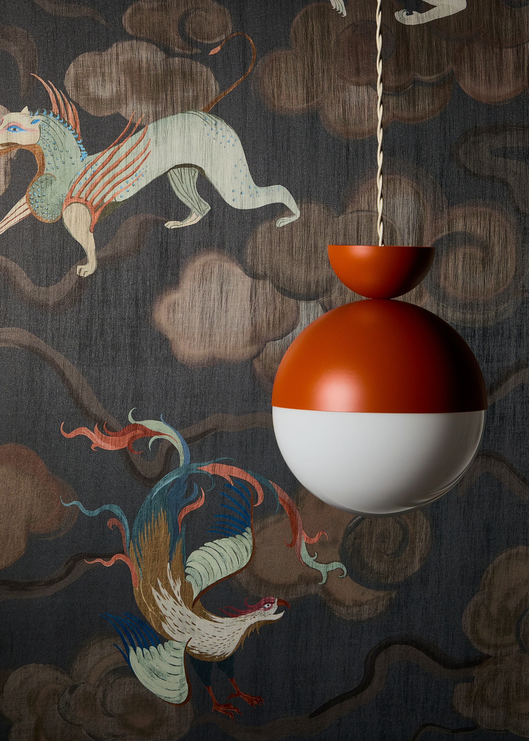 an abstract circle pendant with a half circle upside down on top, half rust orange half white hanging against a mythical creature wallpaper