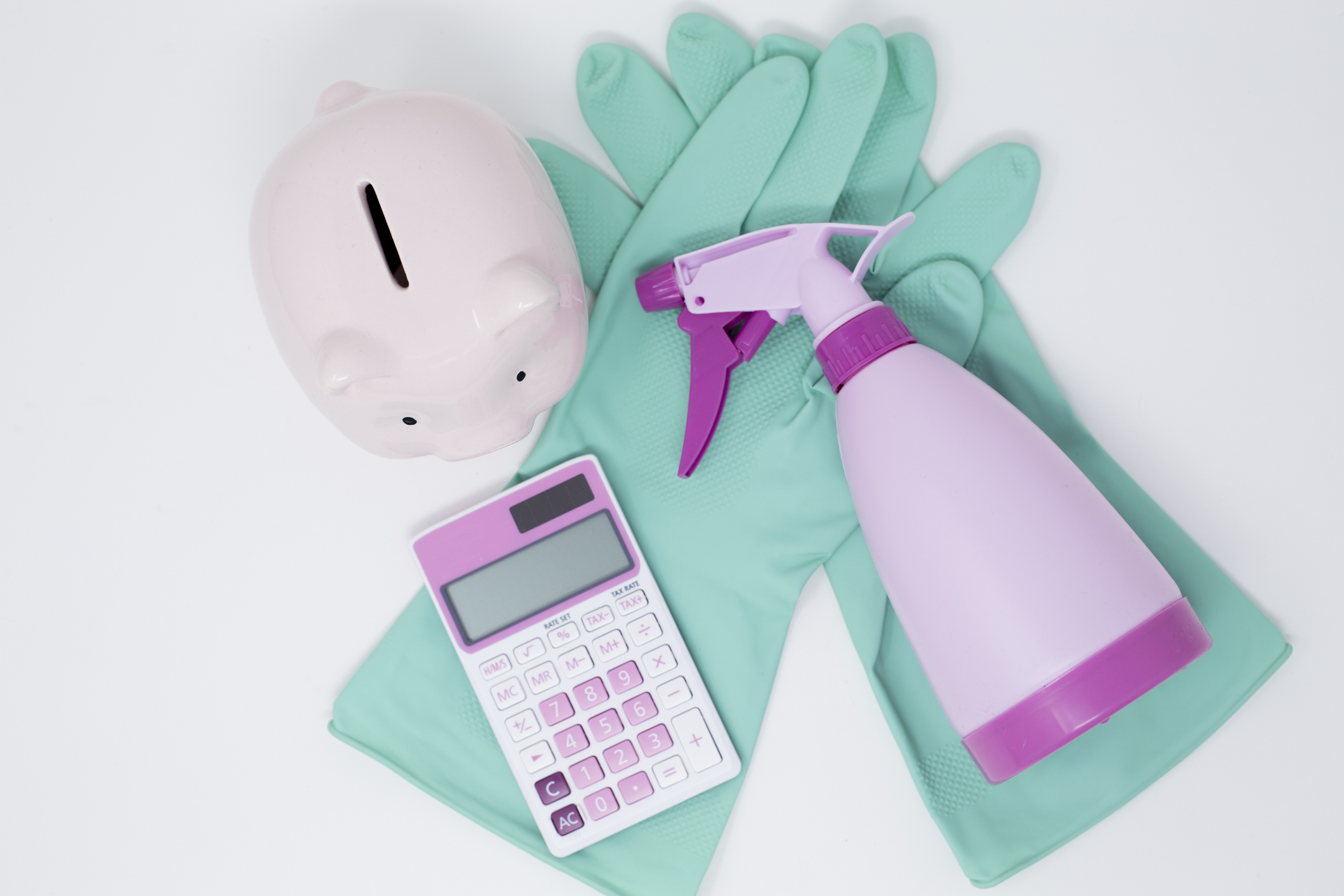 cleaning products in pastel colors, including a pink spray bottle and calculator and teal gloves, next to a light pink piggy bank