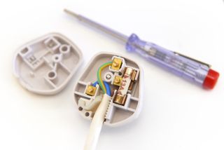 A UK plug open at the back showing the wires and fuse, next to a small screwdriver