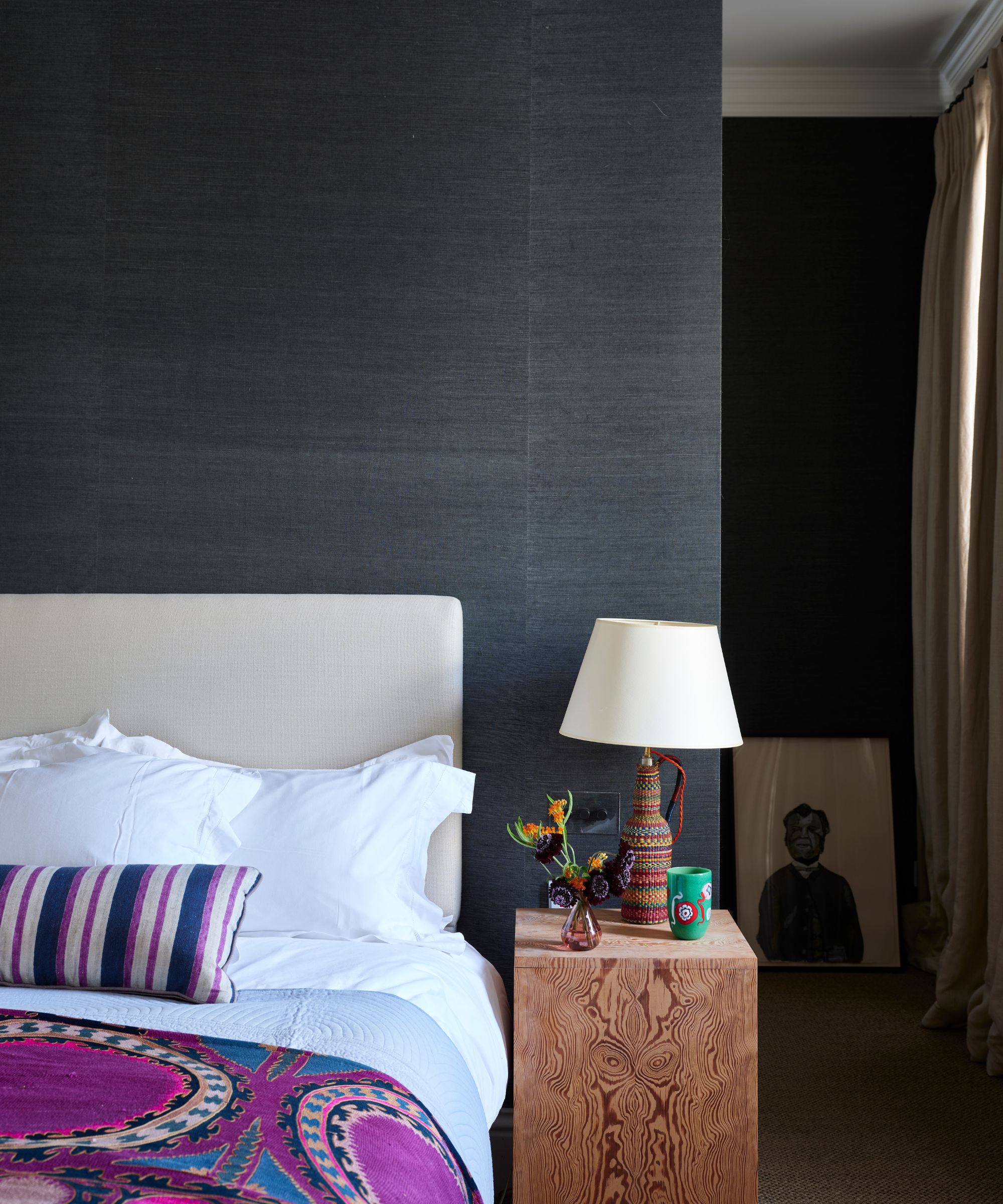 Dark bedroom with purple bedding, wood beside table and woven lamp
