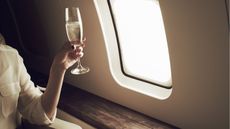 A wealthy woman sits on a private jet with a glass of champagne.