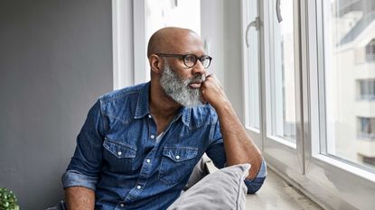 A man looks out a window with a concerned look on his face.