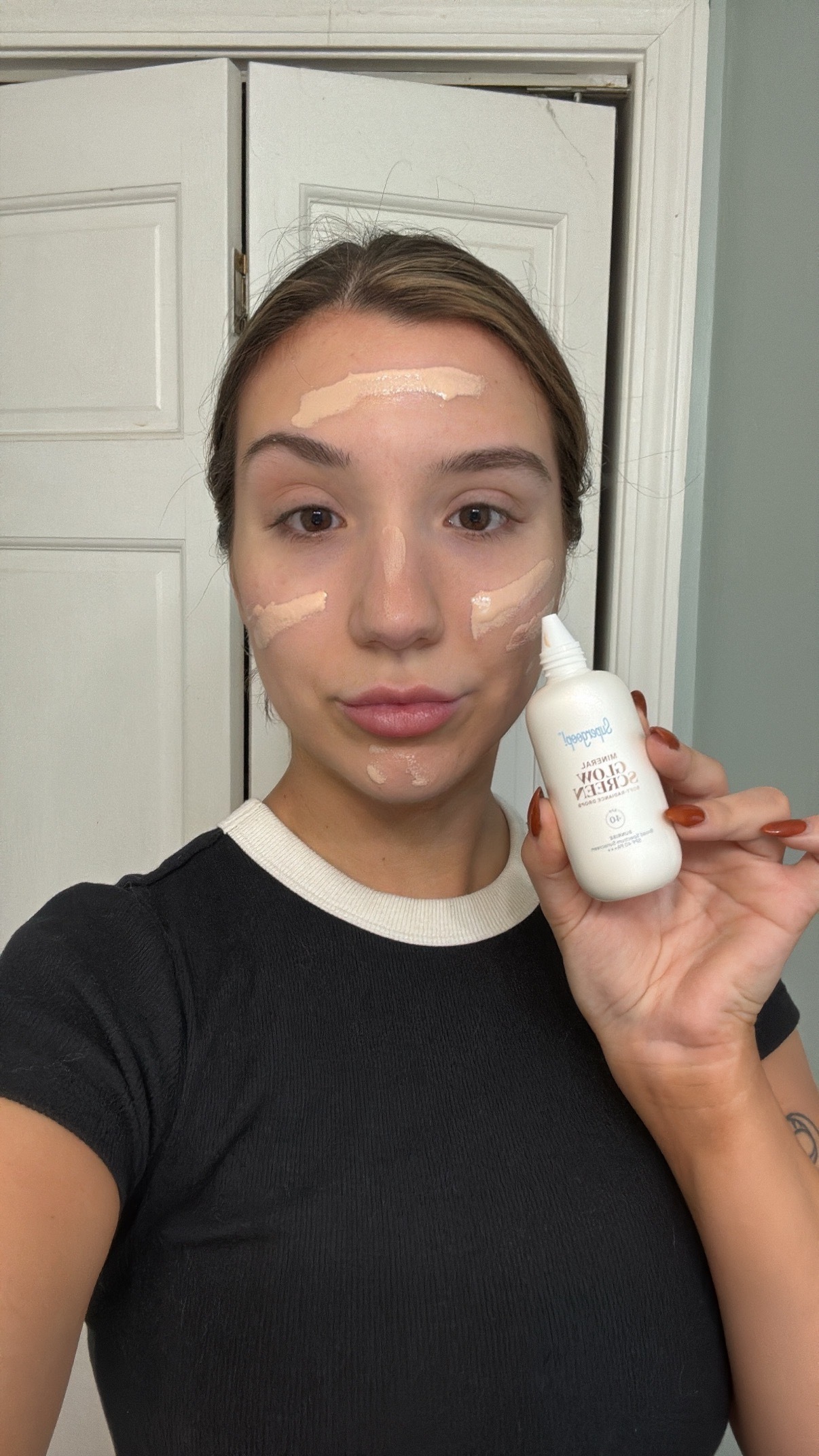 A girl with brown hair and a black shirt before applying spf.