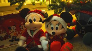 Mickey, Minnie, and Stitch Christmas plush toys under a tree, with a Disney bag beside them