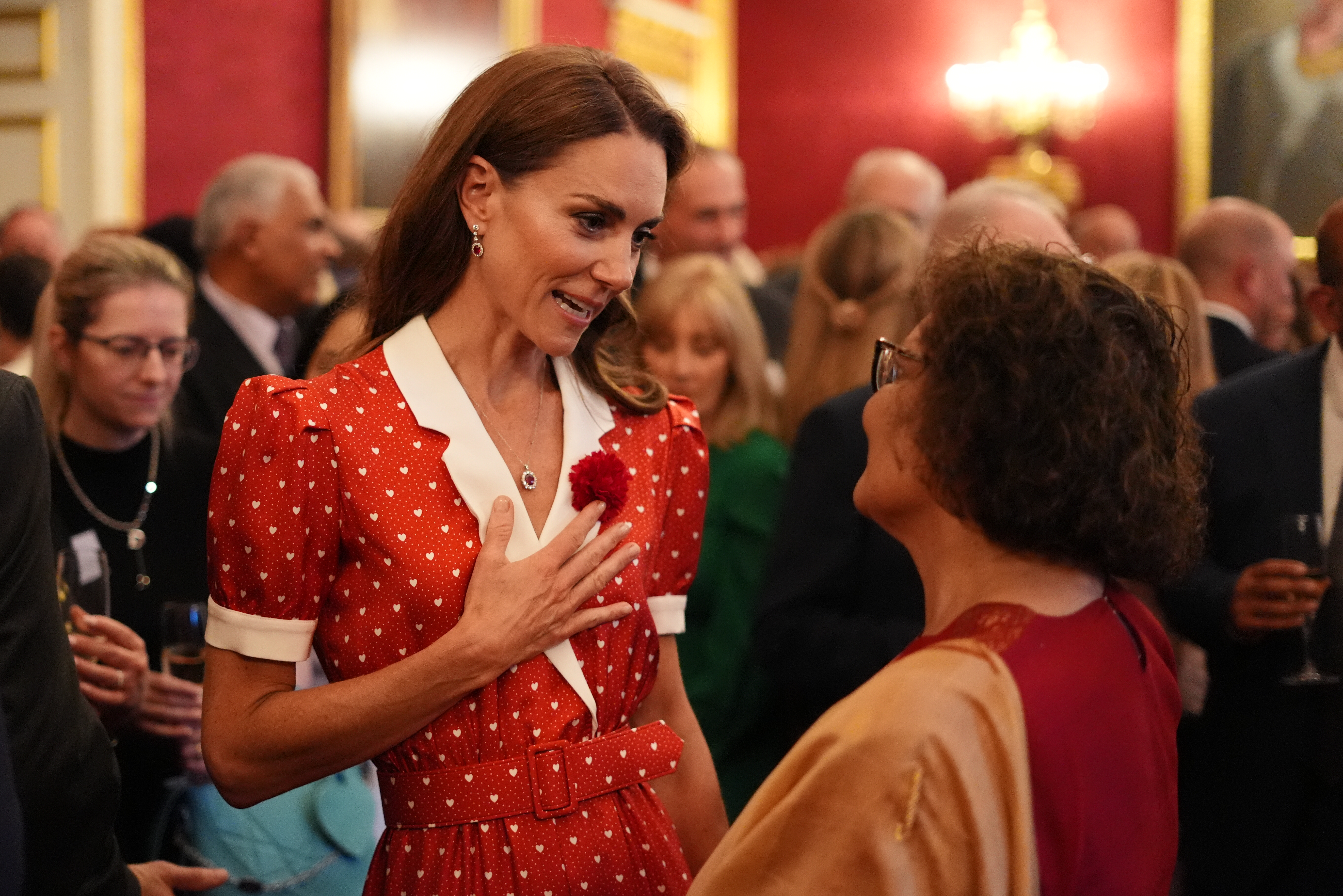 Princess Kate wearing a red heart print dress talking to a woman