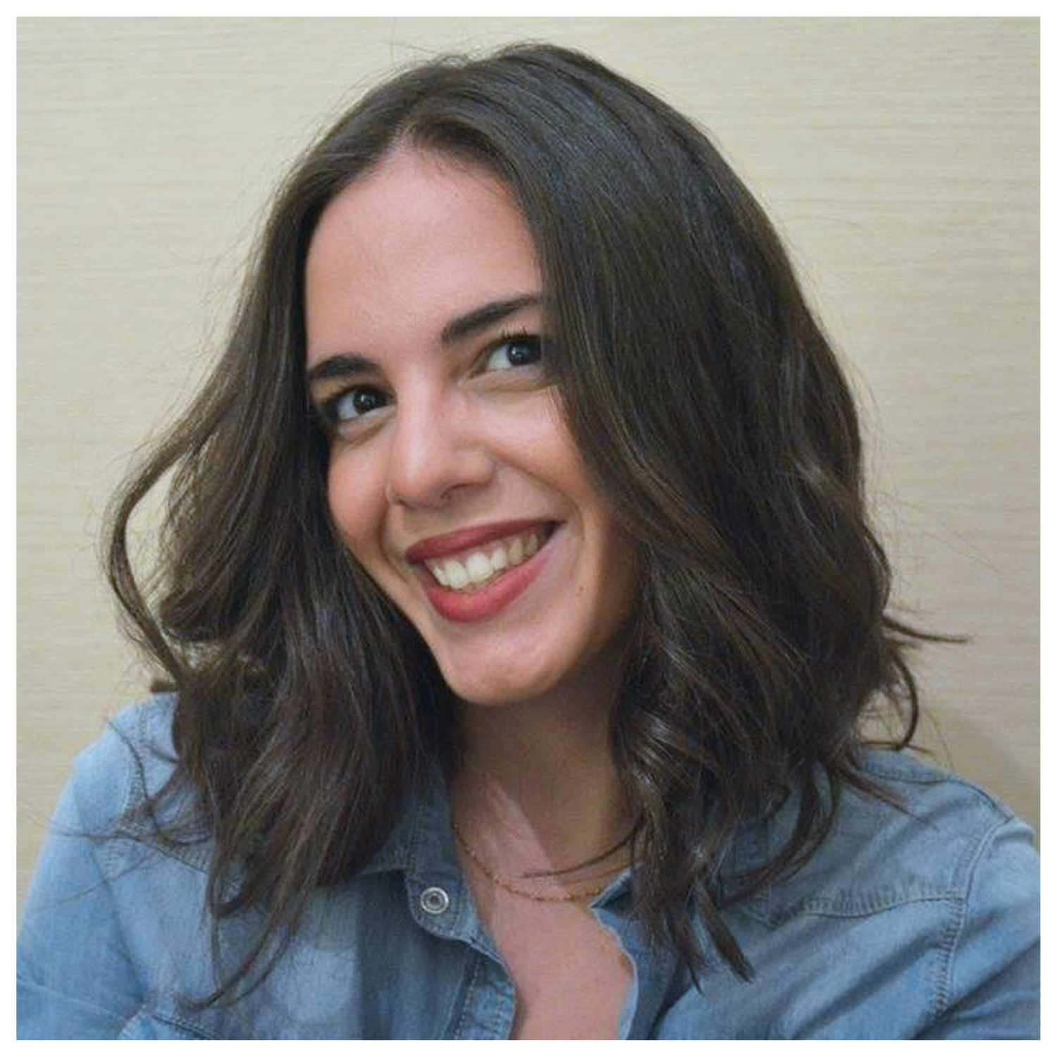 A woman with short wavy brown hair and red lipstick smiling in a denim shirt