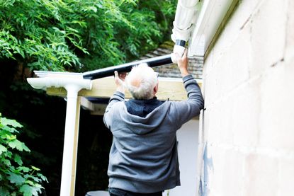 A senior man repairs the downspout on his house.