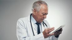 An older doctor looks intently at a tablet.