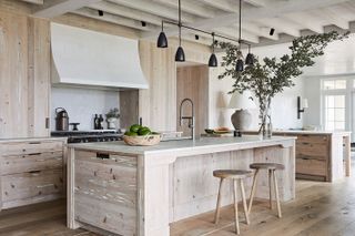 A bright white rustic kitchen with a wooden island and barstools