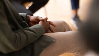 Close-up of a man sitting in a circle during group therapy with his hands clasped.