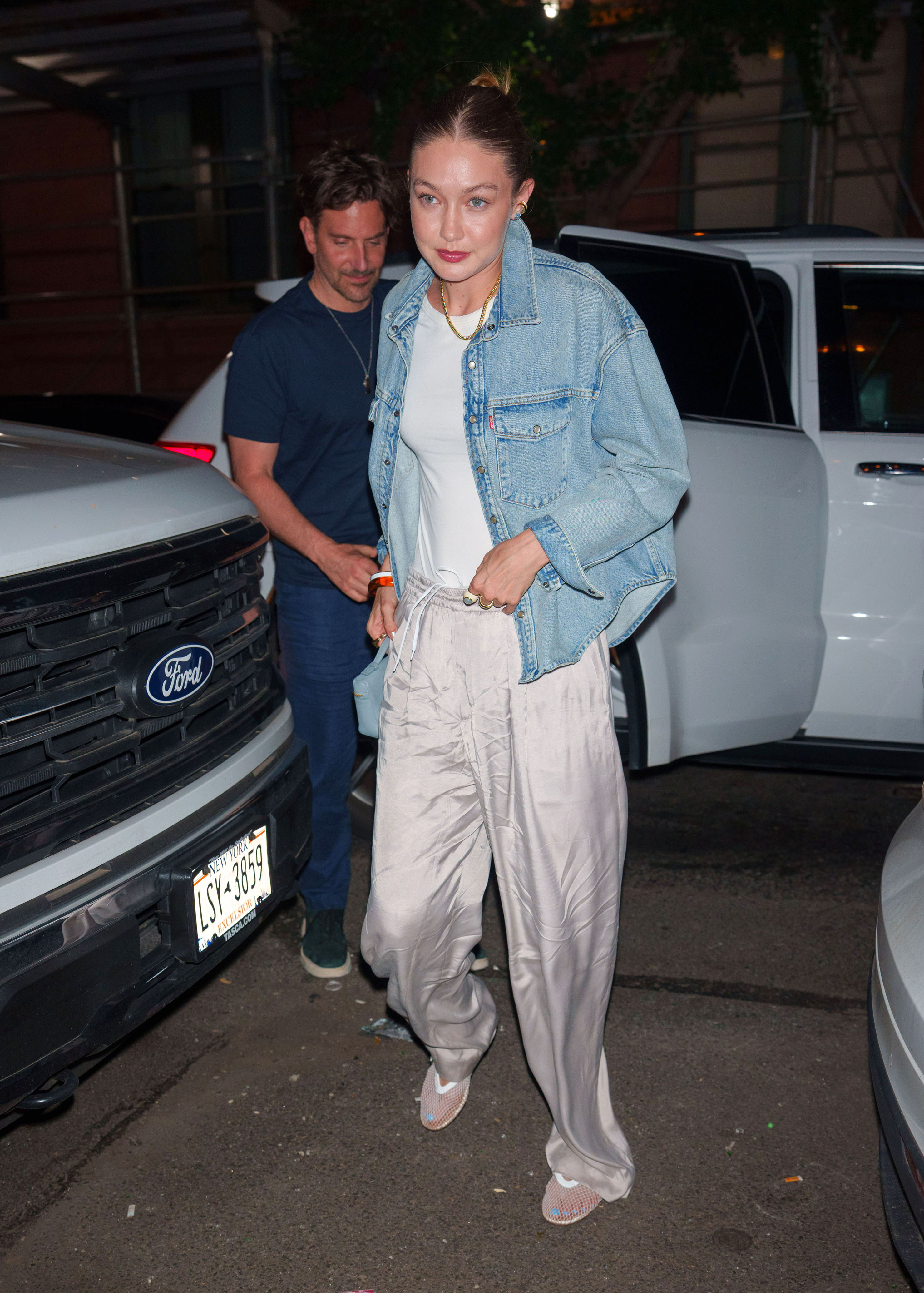 Gigi Hadid wearing a denim jacket, metallic track pants, and mesh flats