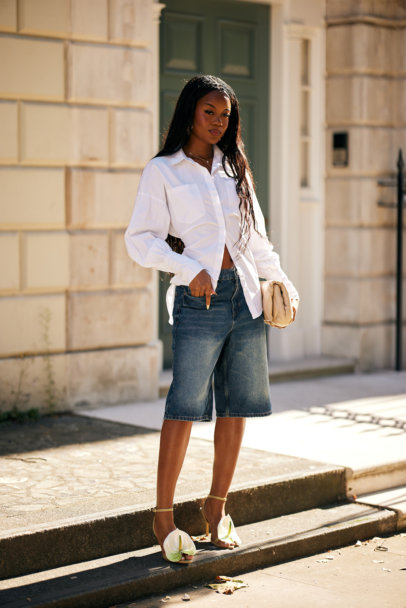 a woman in London wearing a white button-down shirt, denim Bermuda shorts, and green flower heels