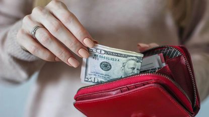 A woman pulls money out of a red wallet.