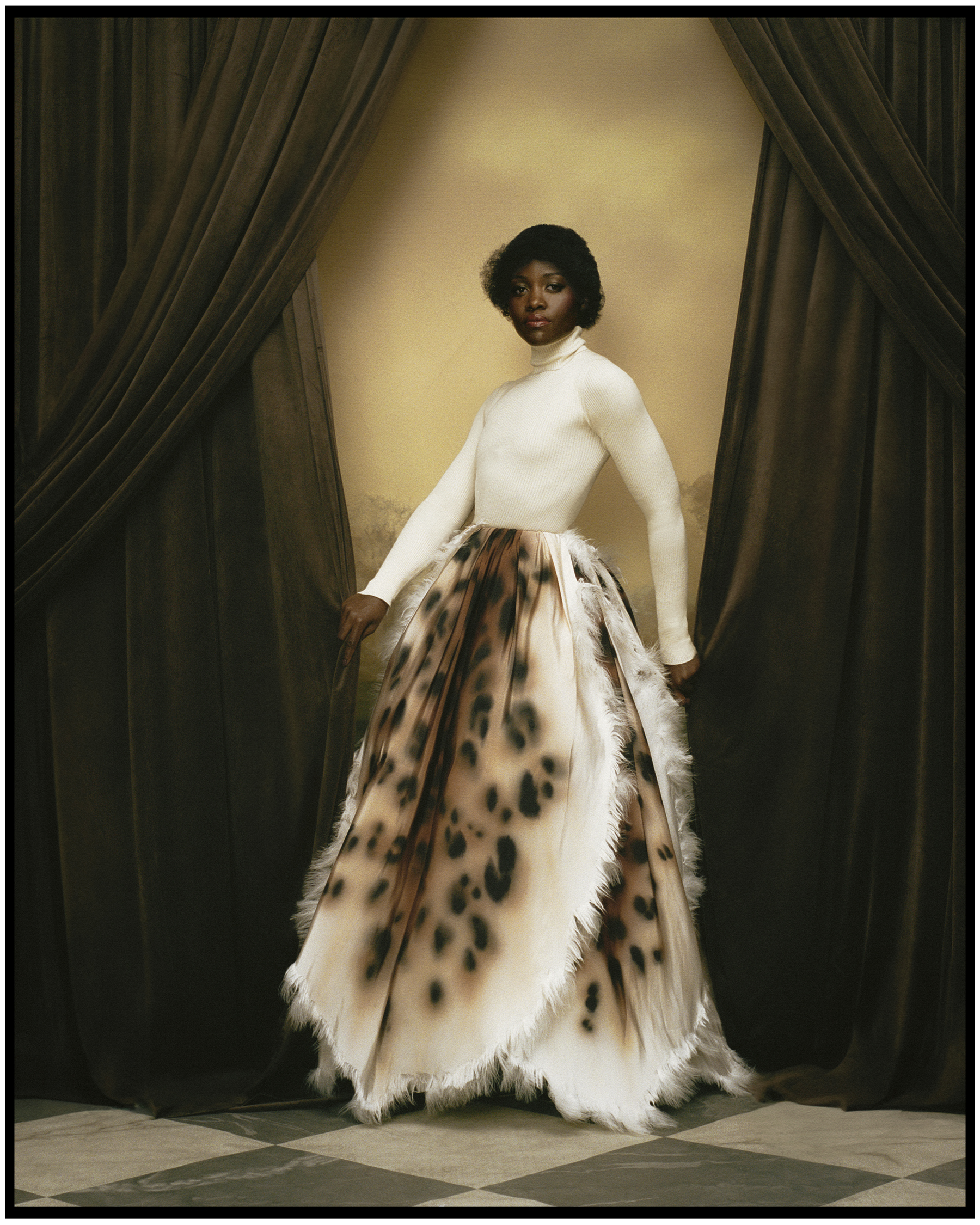 Lupita Nyong'o photographed by Kenny Germe&amp;#769; standing between brown velvet curtains wearing a Chanel white turtleneck tucked into a full skirt with leopard print design.