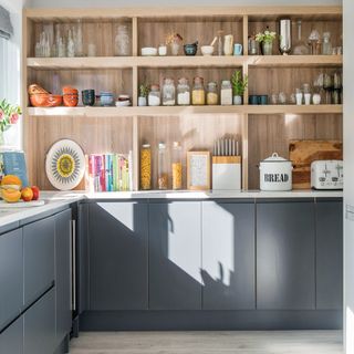 kitchen with grey cabinets and wooden open shelving filled with bowls, glasses and cereal