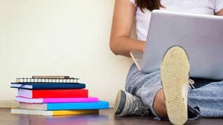 Best student laptops: a person sat on the floor using a laptop next to a stack of books