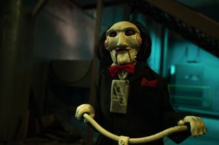 Saw X: Billy the puppet riding a tricycle with a tape player attached to him