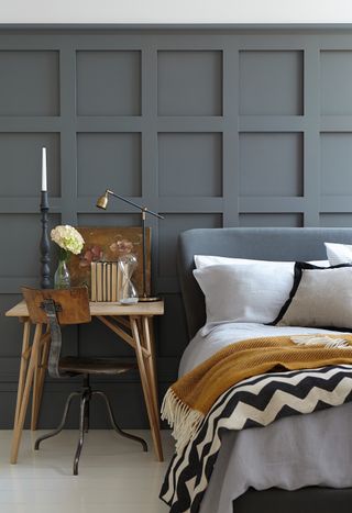 A paneled bedroom painted in grey with grey headboard on bed with mustard and striped throw decor