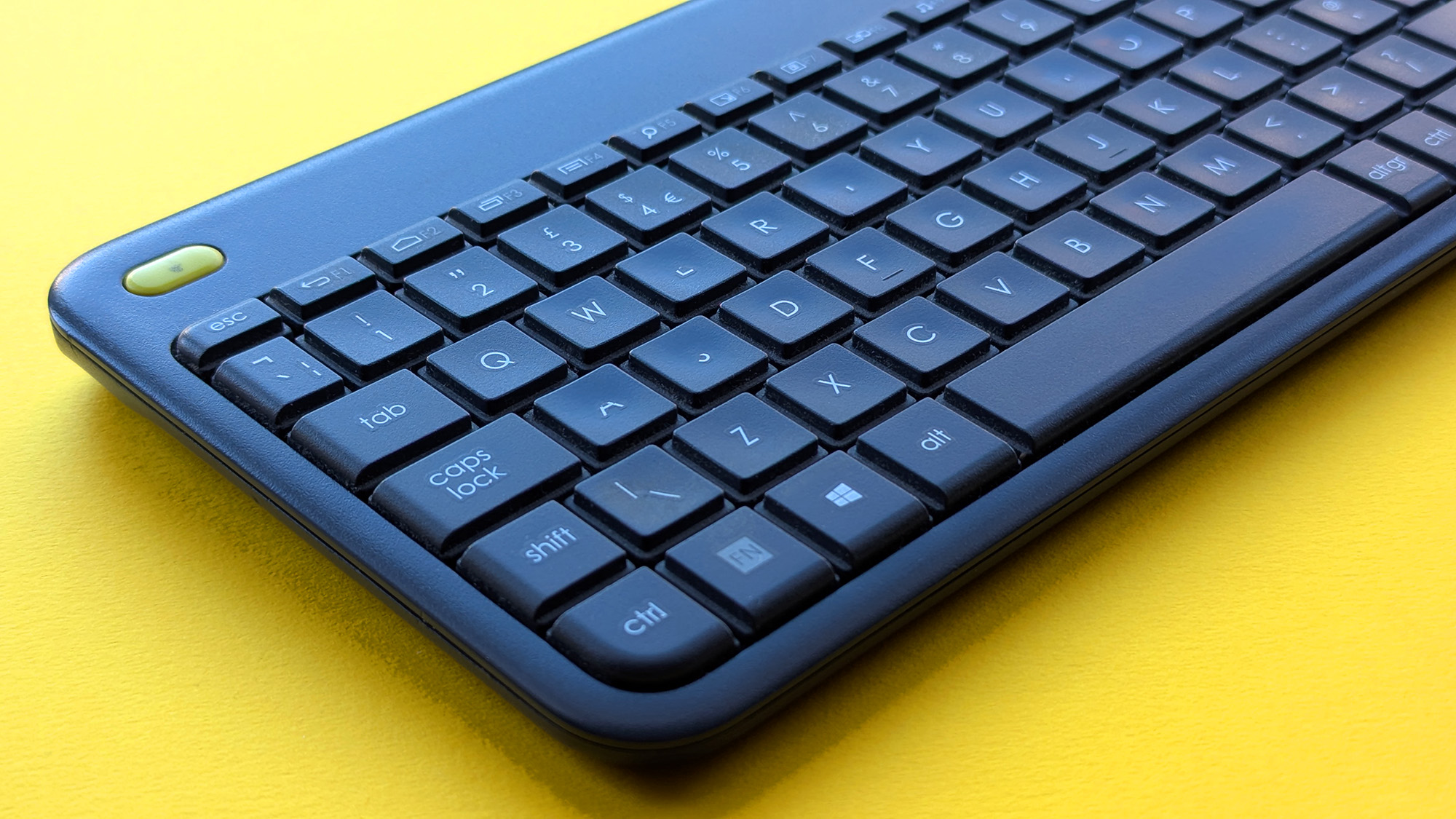 Closeup of Logitech K400 Plus wireless keyboard on a yellow background showing worn keys and buttons