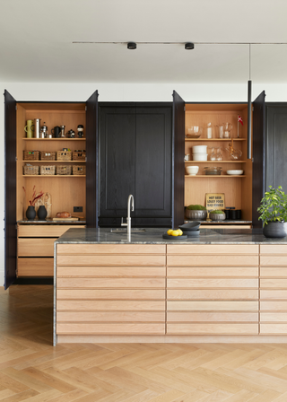 Chic kitchen design with light wood, fluted island and black cabinetry with pocket doors, concealing appliances and accessories